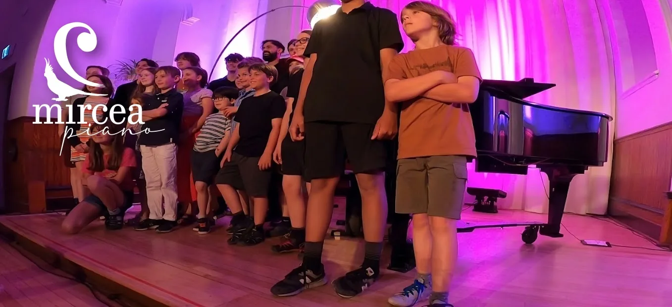 Students lined up on stage before a group concert, grand piano in the background.