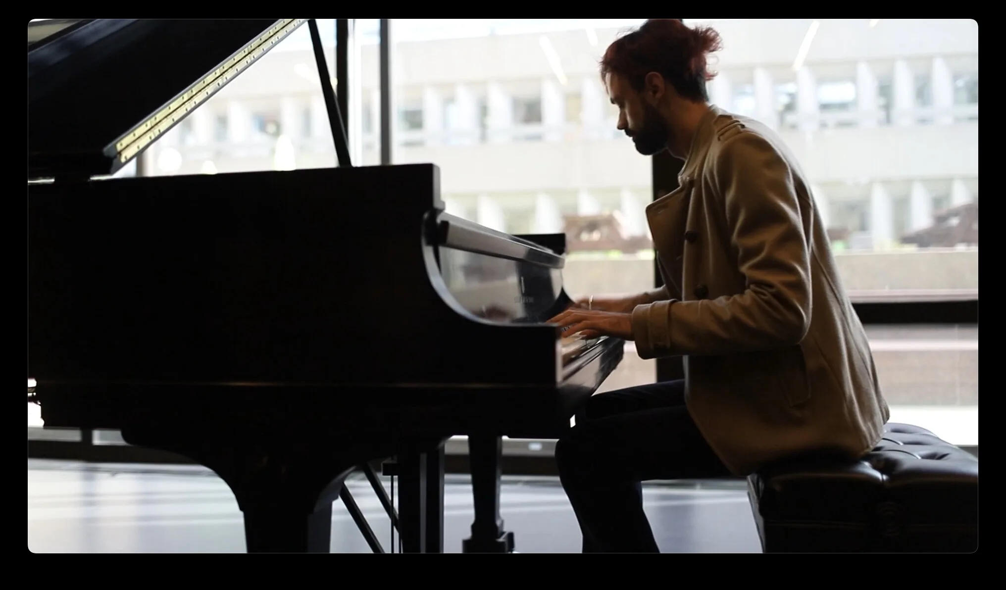 Mircea at the grand piano in front of a large window, mid-performance.