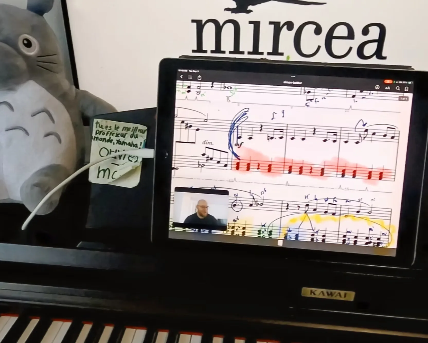Annotated sheet music on a tablet during a lesson, with a note from a student on the piano.
